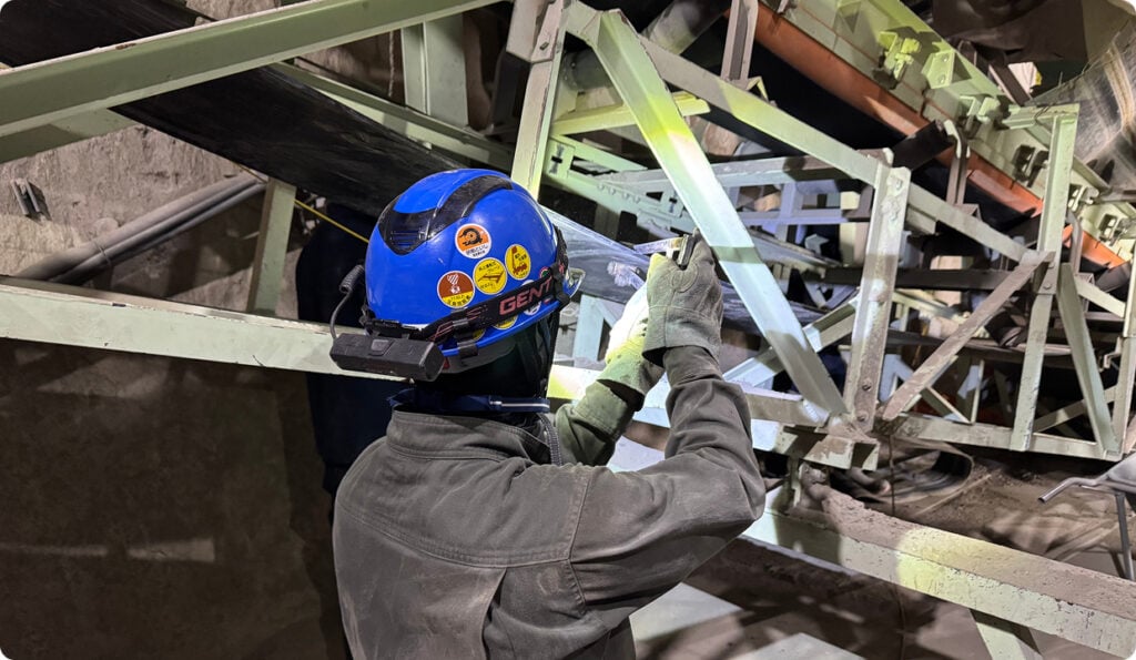 安全ヘルメットを着用した作業員が工場の機械構造を点検している様子.