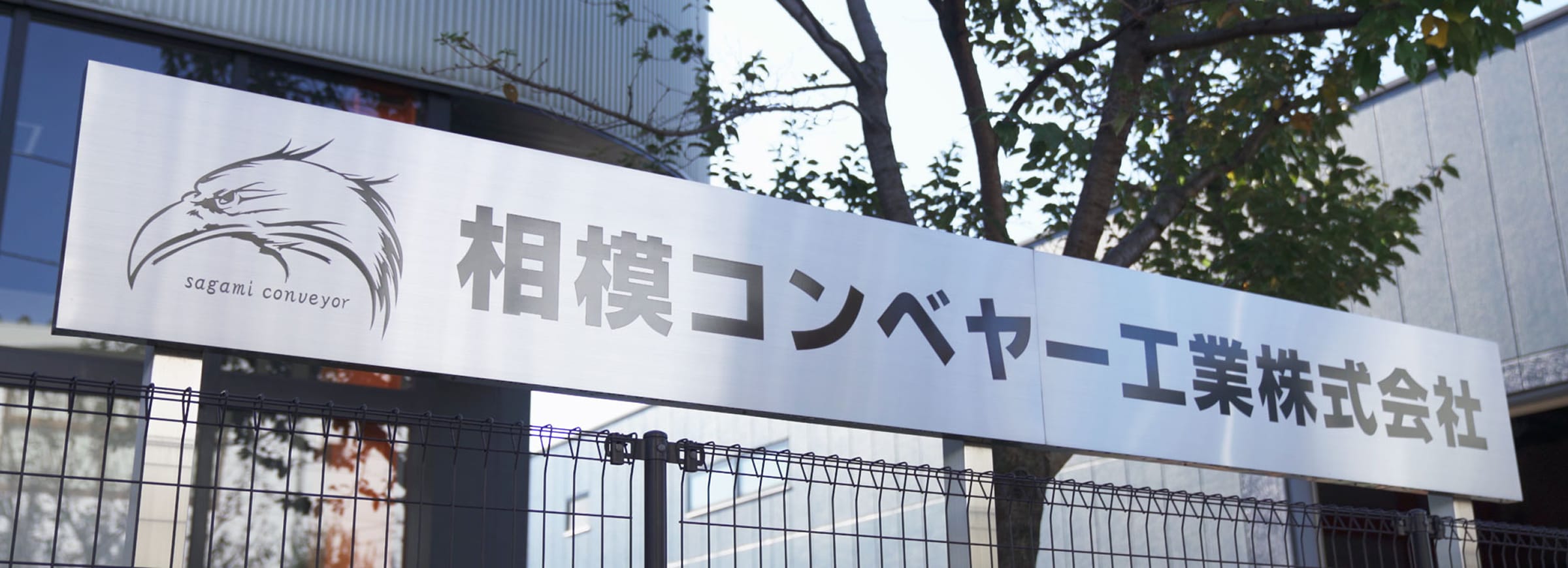 鳥のロゴと「相模コンベヤー工業株式会社」の社名が大きく書かれた、屋外に設置された横長の看板。