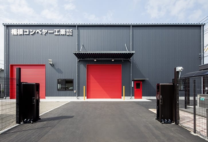 赤いシャッターが特徴的な相模コンベヤー工業株式会社のモダンな工場外観