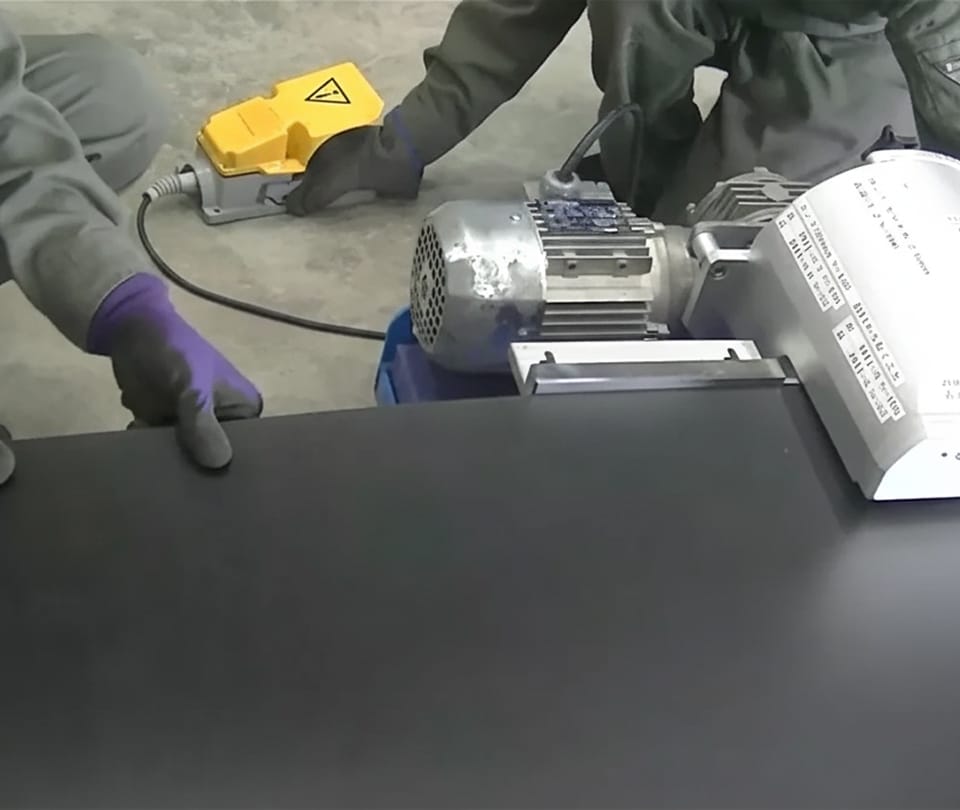 フットスイッチを用いて機械を操作しながら、黒いコンベアベルトの加工を行う作業員の手元