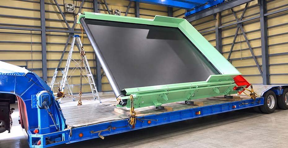 完成した大型コンベアを輸送用トラックの荷台へ慎重に積み込む出荷風景