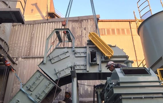 工場屋外で、大型クレーンを使用してグレーのコンベアユニットを慎重に吊り上げ、所定の位置へ設置している工事風景。