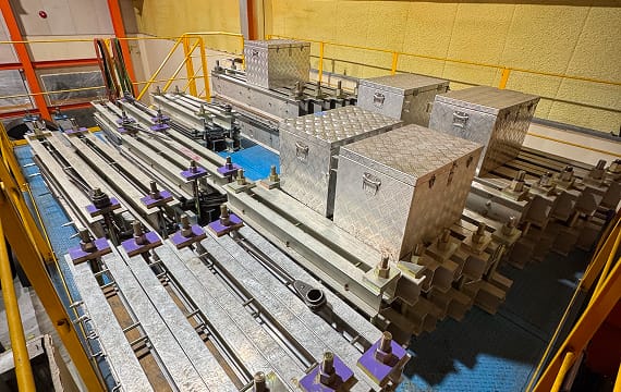 屋内作業場に整然と並べられた、ベルトコンベアの接合作業に使用する大型の金属製プレス機と、アルミ製の機材保管ボックス。