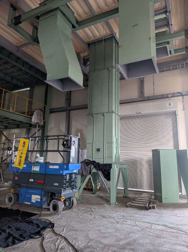 工場内の大型バケットコンベアと作業用リフト。産業用の機械と設備が設置された工場の内部風景。.